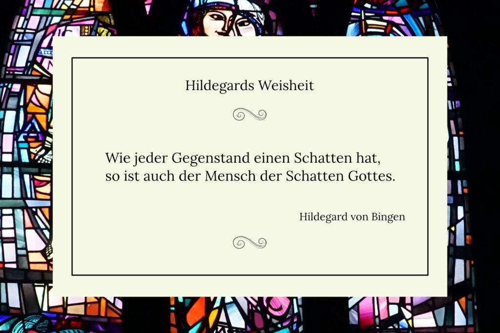 Ich brauche für das Bild einen Alttext. Ein Zitat von Hildegard von Bingen auf einem hellen, rechteckigen Hintergrund vor einem bunten, abstrakten Kirchenfenster aus Glas. Das Zitat lautet: „Wie jeder Gegenstand einen Schatten hat, so ist auch der Mensch der Schatten Gottes.“ Oben steht „Hildegards Weisheit“, unten rechts „Hildegard von Bingen“. Das Bild vermittelt eine spirituelle und nachdenkliche Atmosphäre.
